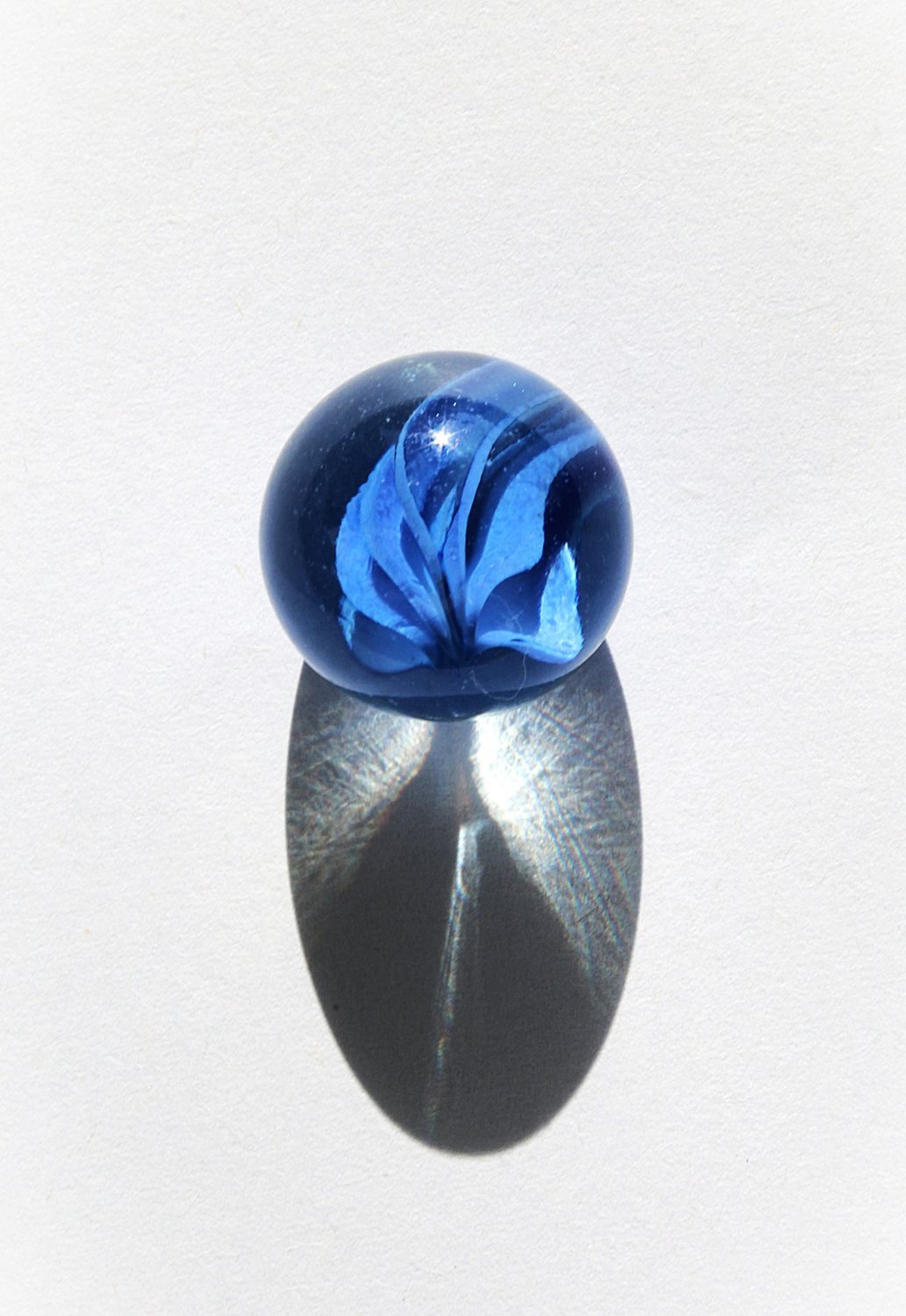 Blue glass marble casting a long shadow on white paper
