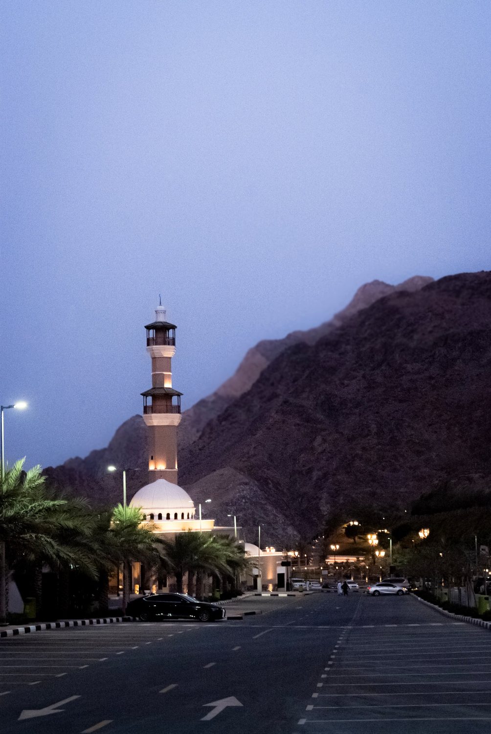 A lit minaret against a mountain ridge at blue hour, Oman