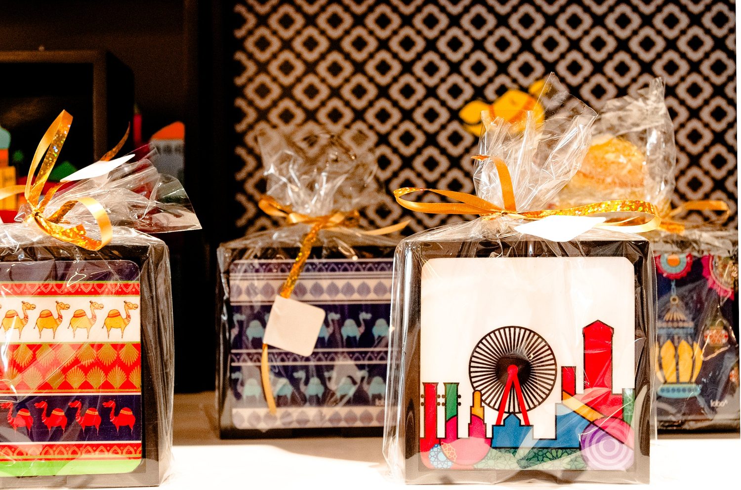 Gift-wrapped coaster sets with illustrated Dubai and camel designs on a shelf